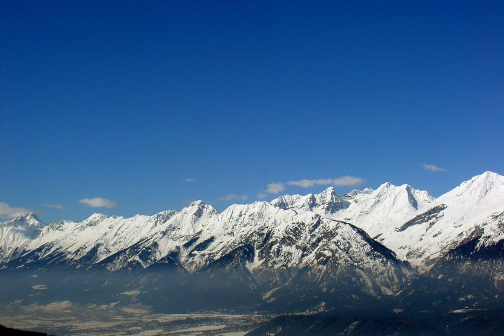 Breathtaking panoramic view of snow-covered alpine mountains under a clear blue sky in winter.